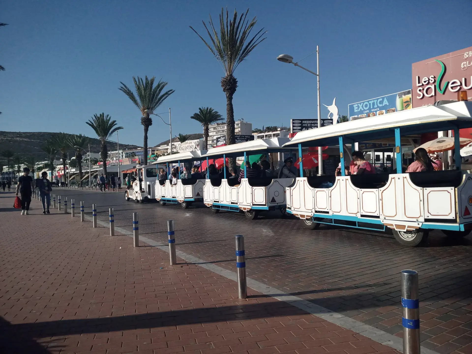 Tourist road train carrying visitors along the palm-lined Agadir seaside promenade