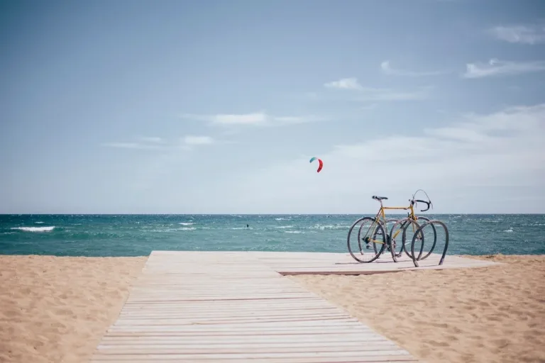 Bicycles parked at a rack on a wooden boardwalk overlooking the beach and ocean on a sunny day