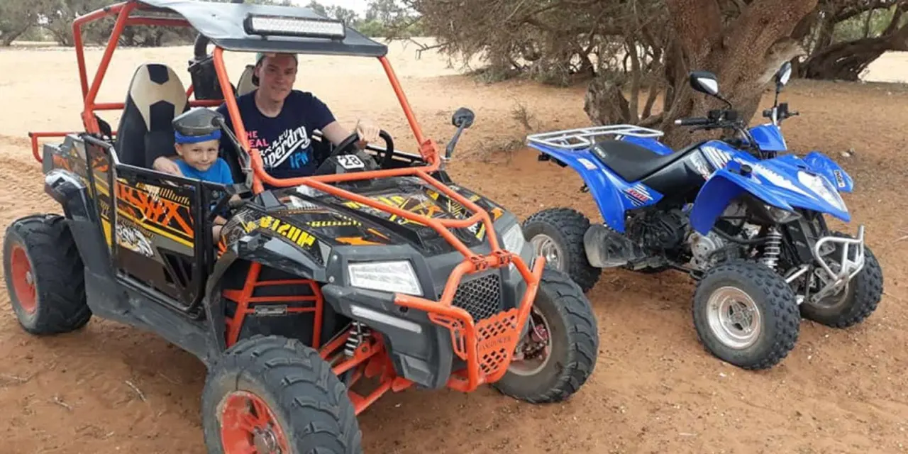 Off-road buggy climbing a golden sand dune under a clear blue sky during a desert tour near Agadir