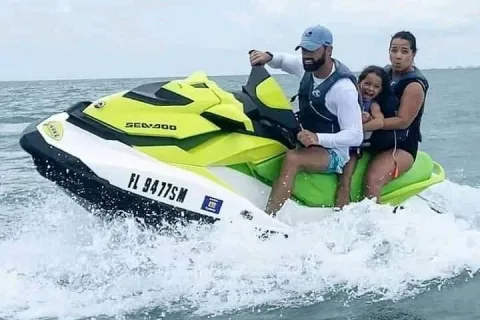 A family of three riding a jet ski at speed, spray kicking up around the hull on a calm sea
