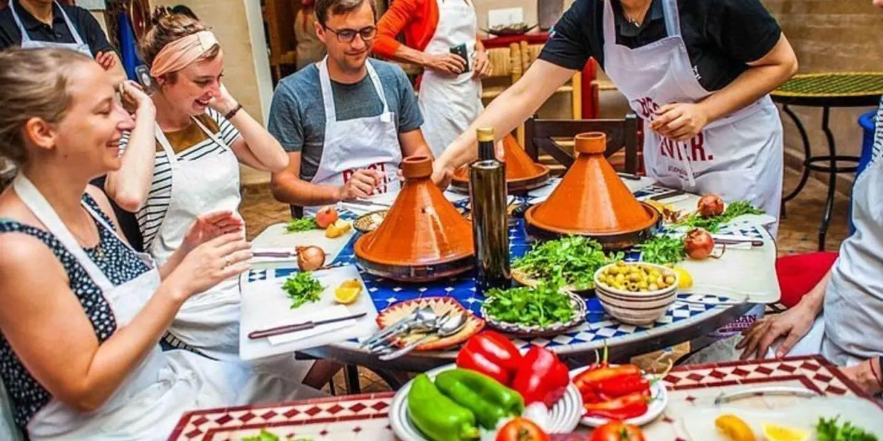 Cooking class guests laughing around a table of tagine pots and fresh vegetables in Agadir