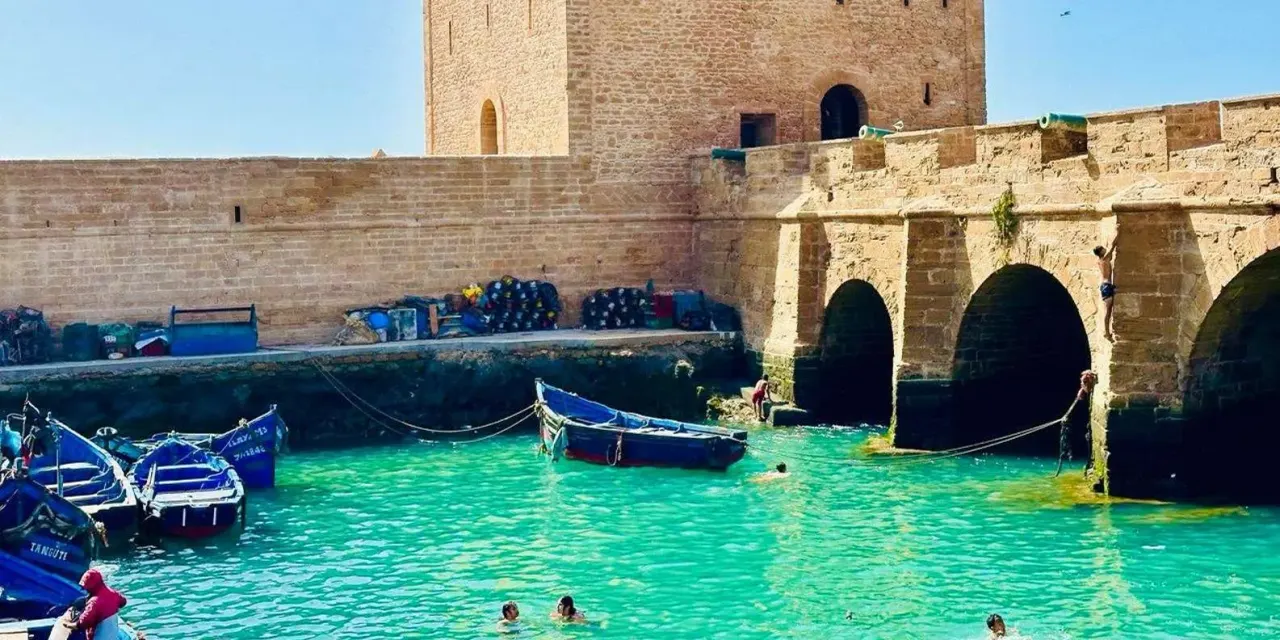 Essaouira's stone port ramparts and blue fishing boats on turquoise water under a sunny sky