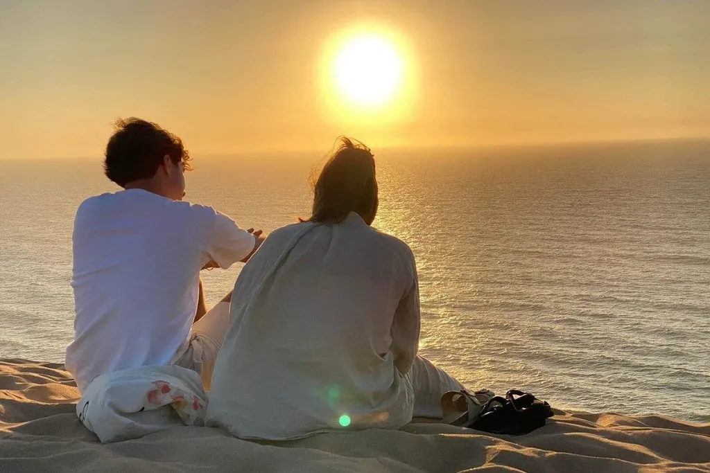 A couple sitting together on a clifftop above the ocean watching the sun set at Timlaline