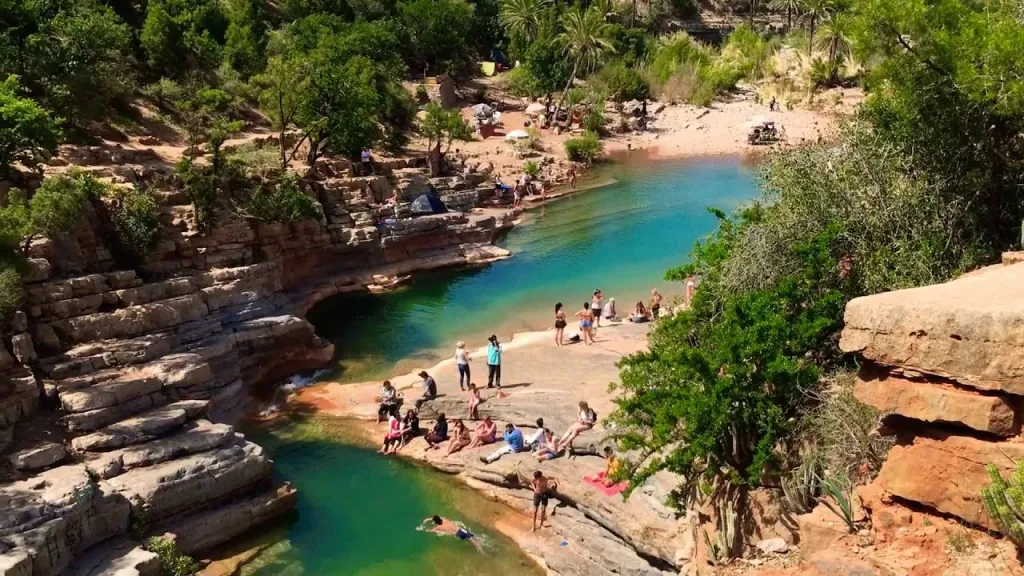Turquoise natural pools of Paradise Valley surrounded by rocky terraces and palm trees with visitors swimming and relaxing
