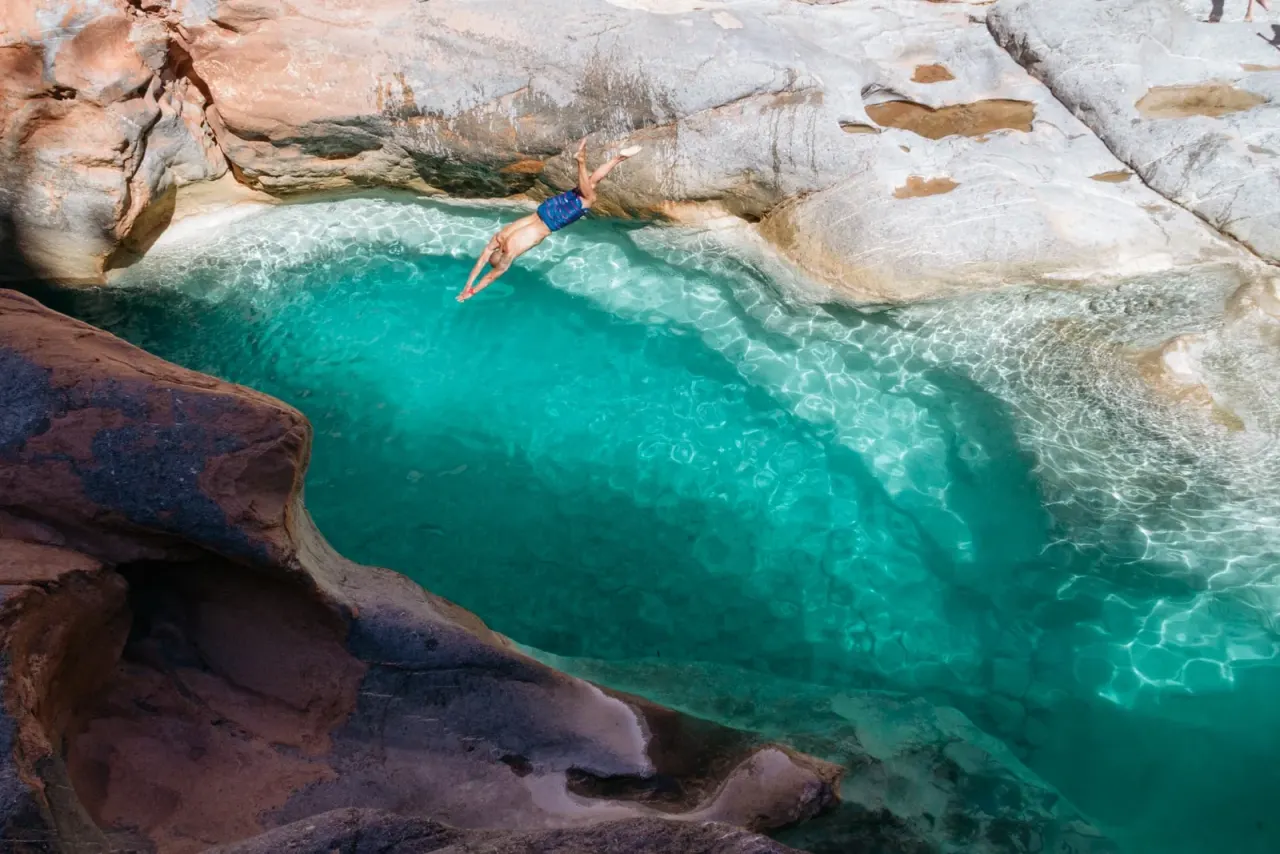 A swimmer diving off a rock into the turquoise pools of Paradise Valley