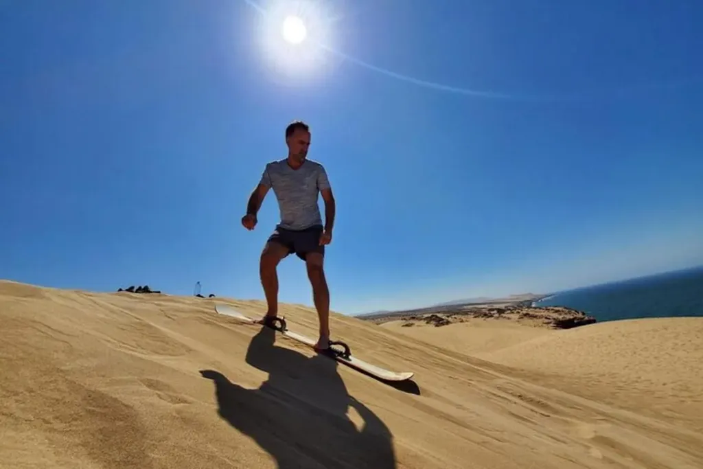 Sandboarder gliding down the golden dunes of Timlaline with the Atlantic coastline in the distance