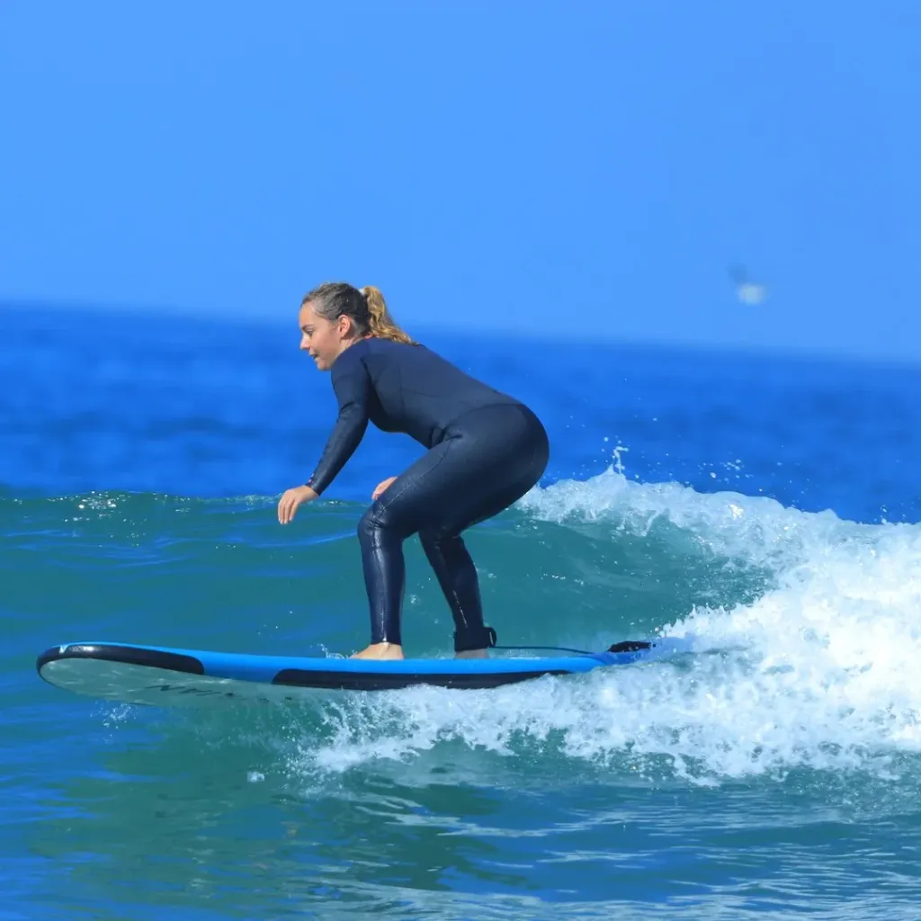 A surfer in a black wetsuit standing on a blue surfboard riding a turquoise wave at Agadir beach