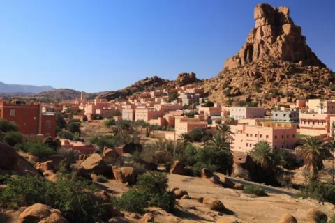 A massive pink granite rock formation rising above the town of Tafraout with its rose-coloured houses and palm trees