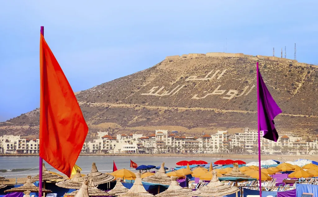 Agadir's beachfront with straw umbrellas and the Agadir Kasbah hill overlooking the bay
