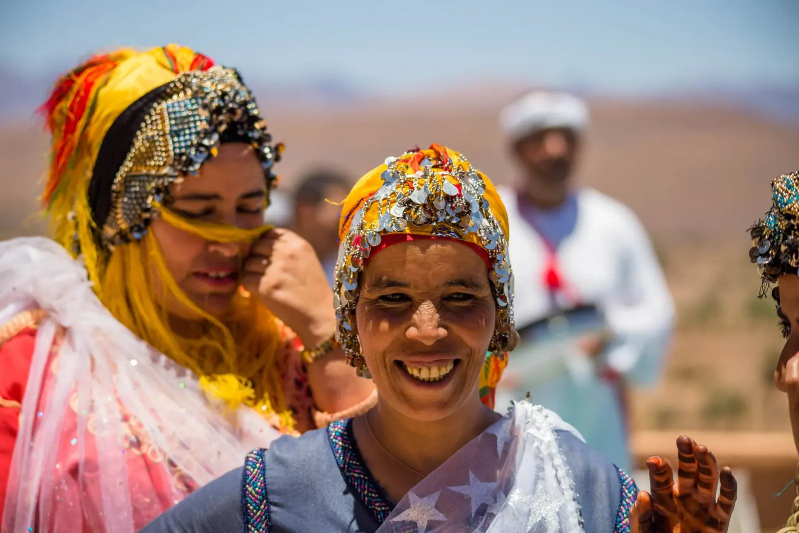 Smiling Berber woman wearing a traditional coin-decorated headdress and colourful dress at an outdoor gathering